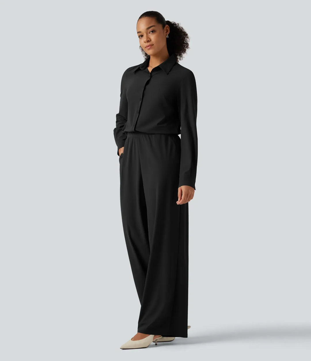 Sida av kvinna i långärmad svart jumpsuit med fickor
