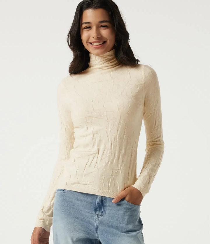 Beige damtröja med hög hals och långa ärmar, helfigur