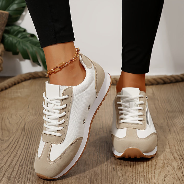 Beige dam sneakers med snörning och vit sula på trägolv