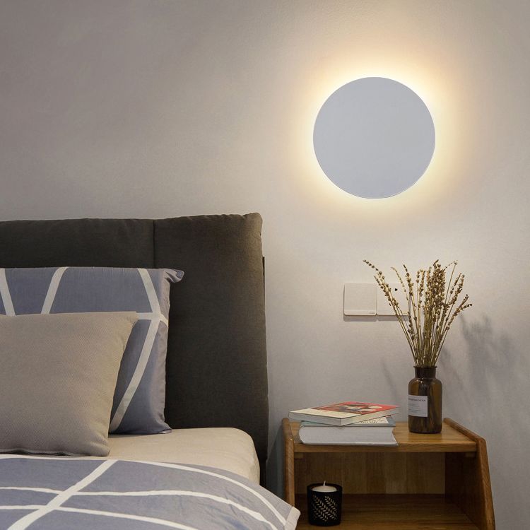 Vit rund LED-vägglampa ovanför ett sängbord i ett sovrum