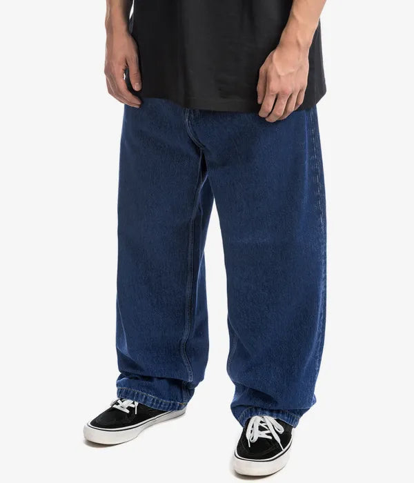 Man bär mörkblå loose fit jeans med svarta sneakers
