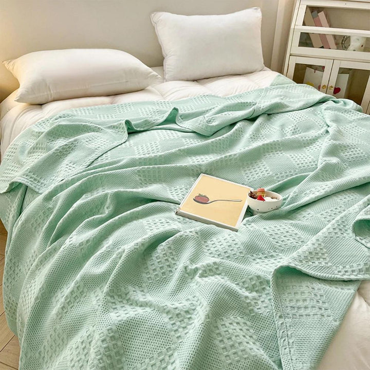 Grönt vaffelfilt draperat på en bäddad säng med bok