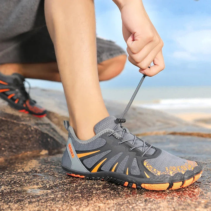 Grå vattenskor med orange detaljer på stenig strand