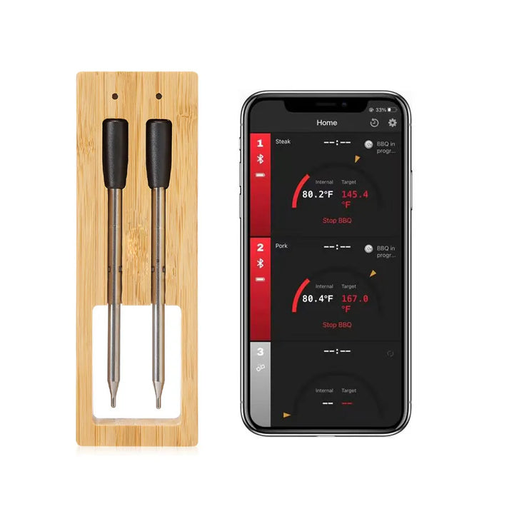 Dubbla sondspetsar i bambuhållare bredvid en smartphone som visar temperaturer för flera köttstycken