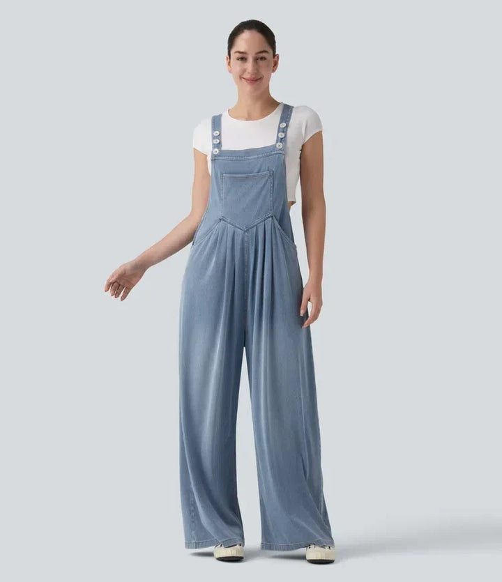 Kvinna i blå draperad baggy overall framifrån med justerbara axelband och fickor