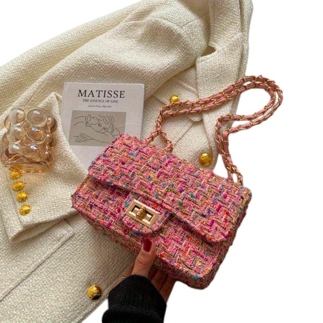 Olivia elegant rosa handväska med kedjerem hållen i handen framför ljus jacka
