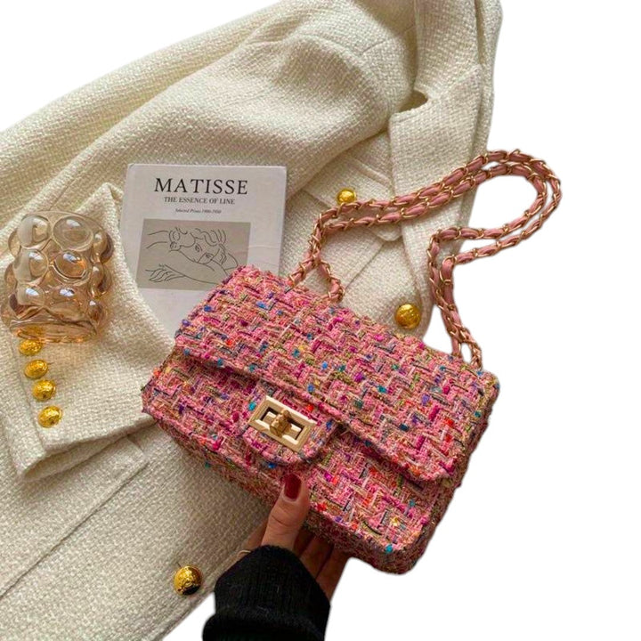Olivia elegant rosa handväska med kedjerem hållen i handen framför ljus jacka