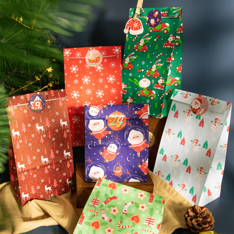Flerfärgade julklappspåsar med julmotiv uppställda bredvid gran
