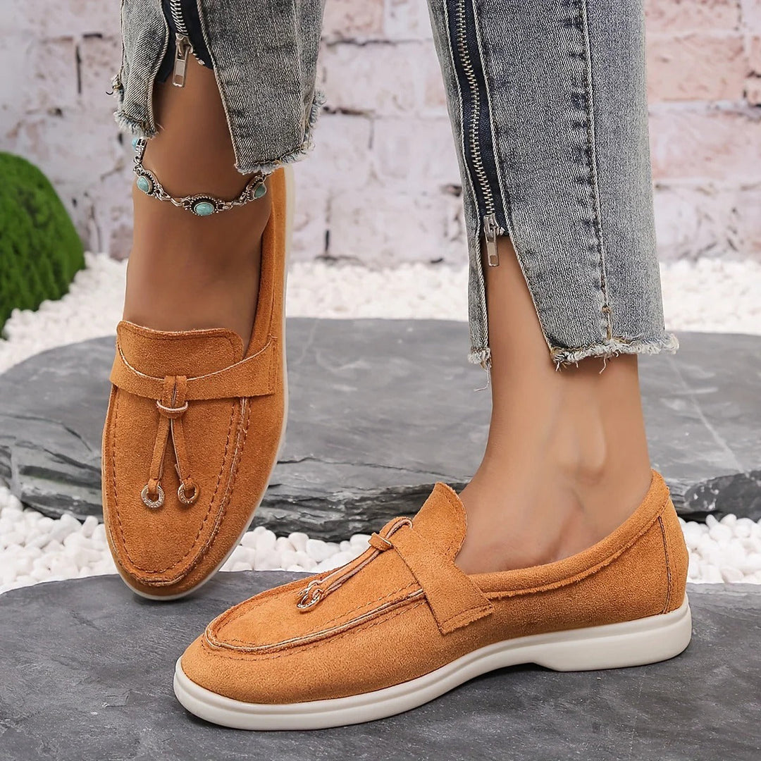 Orange damloafers med dekorativ detalj på stenig yta