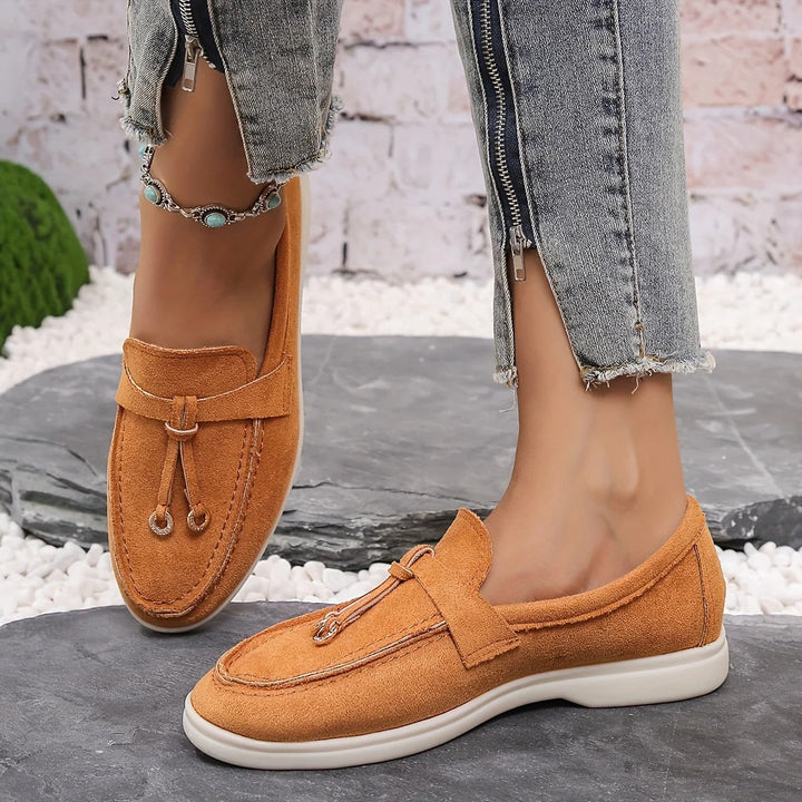 Orange damloafers med dekorativ detalj på stenig yta