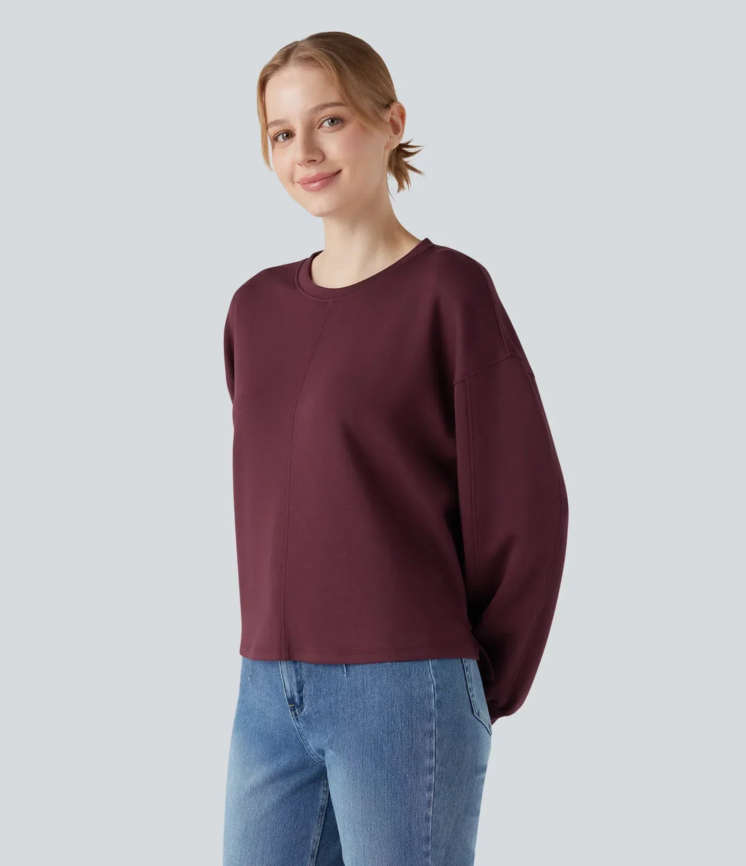 Kvinna i mörkröd sweatshirt i profil med händerna bakom ryggen