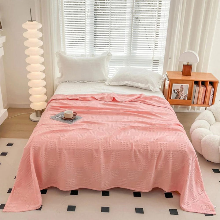 Rosa vaffelfilt på säng i ett ljust rum med modern lampa