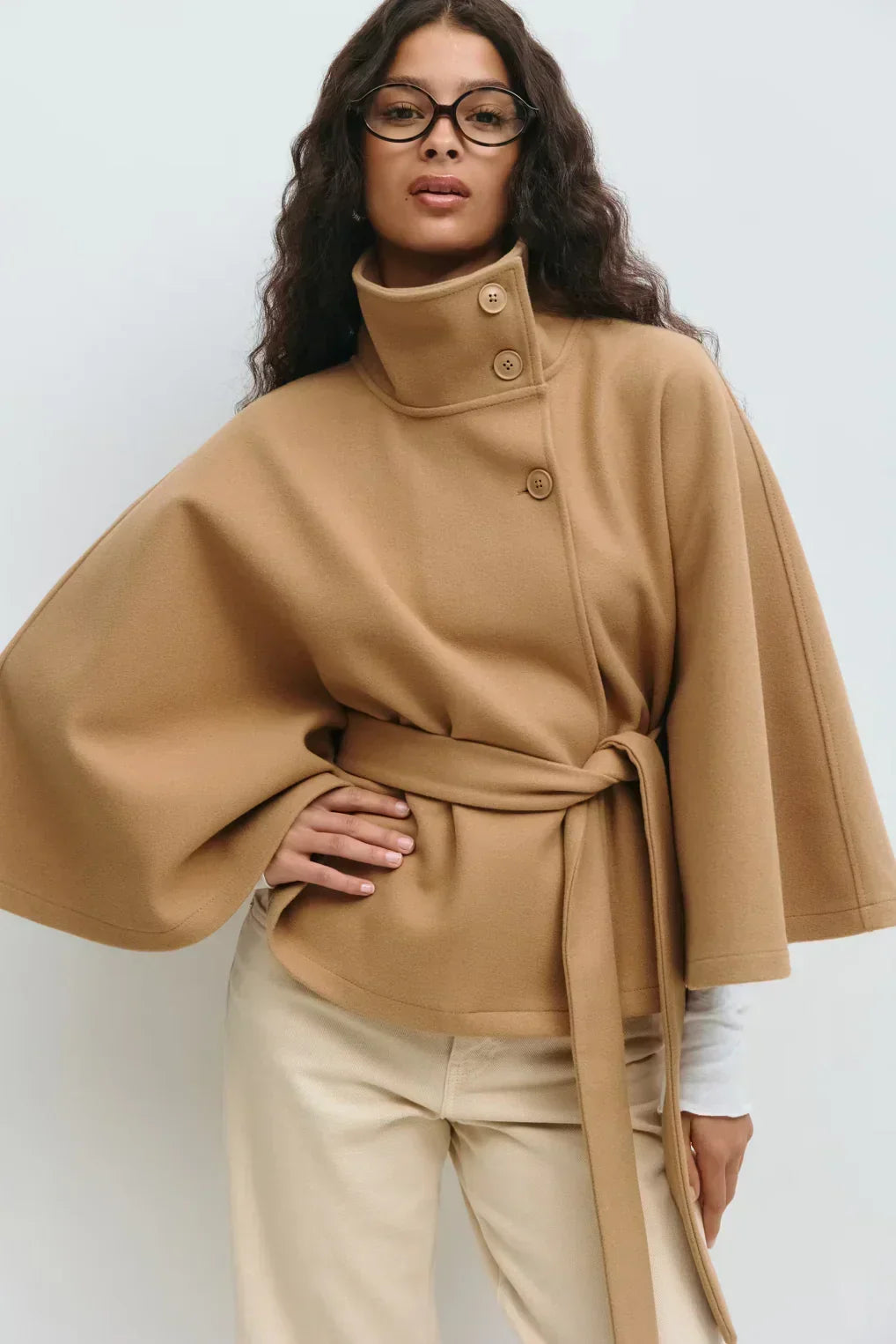 Kvinna i beige capejacka med knytskärp och hög krage