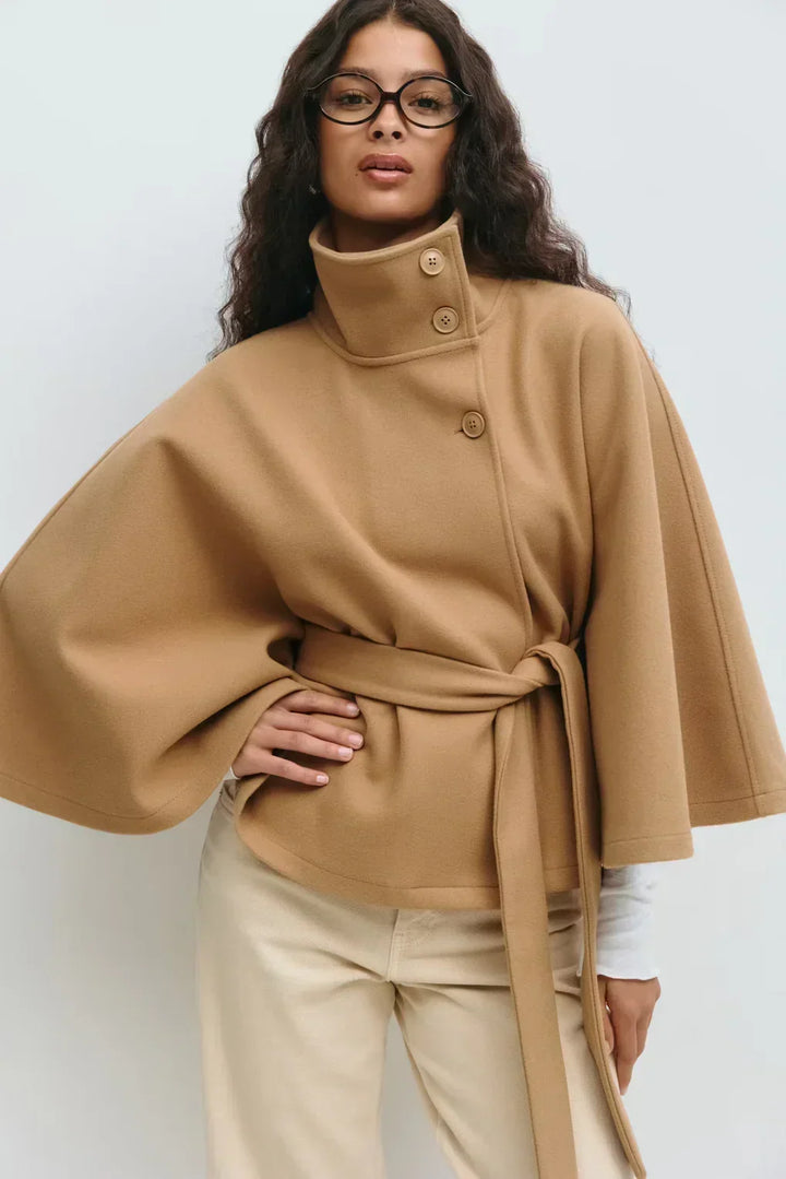 Kvinna i beige capejacka med knytskärp och hög krage