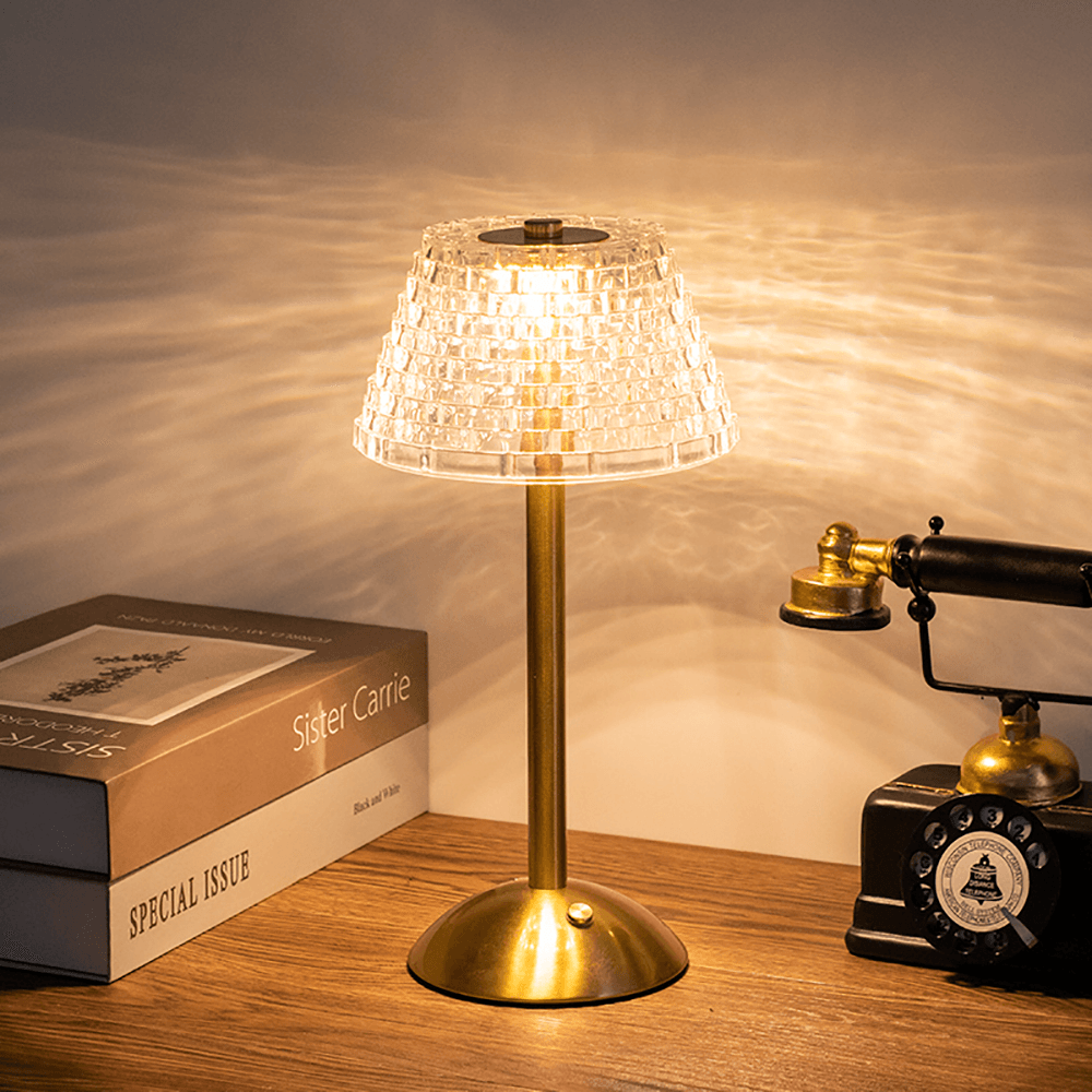 Glimmer trådlös bordslampa i guld placerad på ett bord bredvid böcker och en retrotelefon