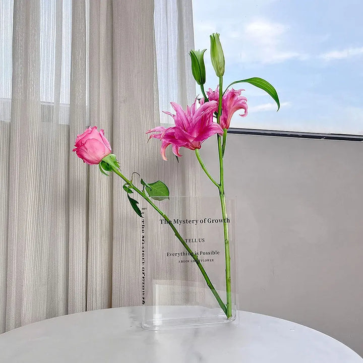 Transparent bokinspirerad blomvas placerad på ett bord med rosa blommor