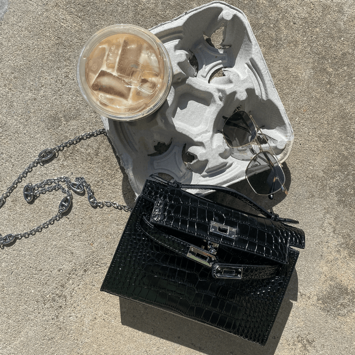 Svart Fauve axelväska liggande bredvid solglasögon och iskaffe