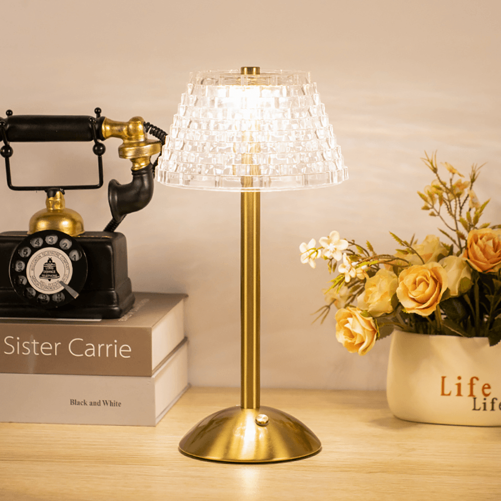 Glimmer trådlös bordslampa bredvid en vas med gula blommor och böcker
