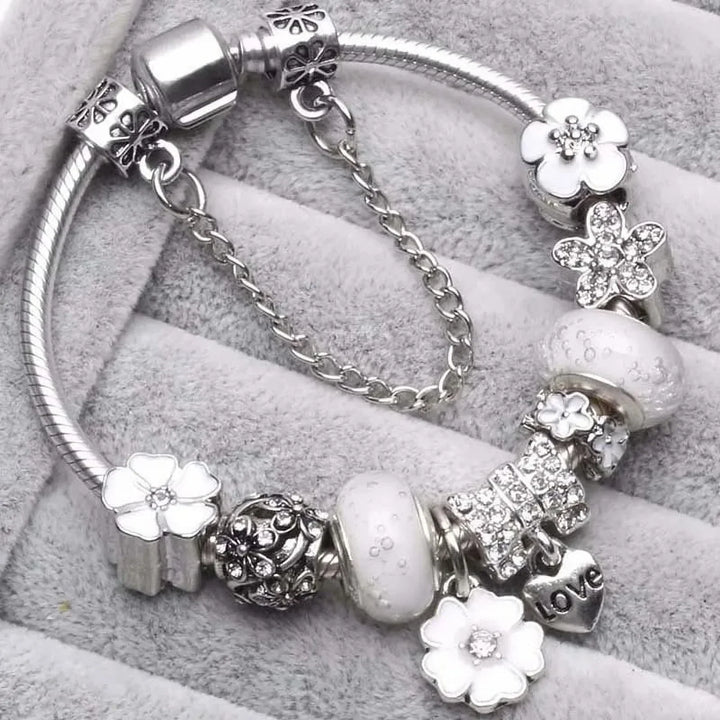Närbild på vitt charm-armband med blommor och hjärthänge