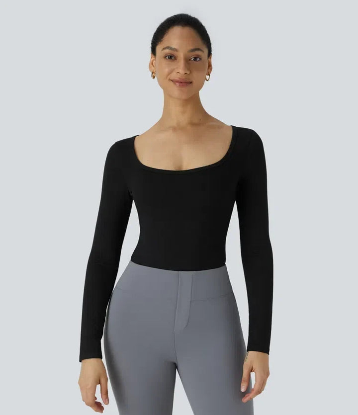 Modell som bär svart långärmad body tillsammans med grå byxor