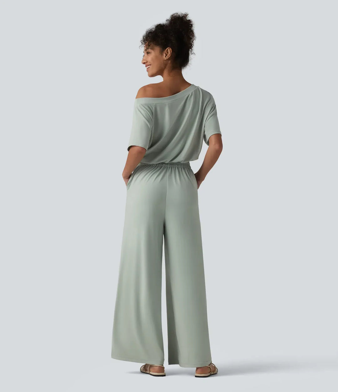Baksidesvy av dam i ljusgrön baggy jumpsuit med korta ärmar