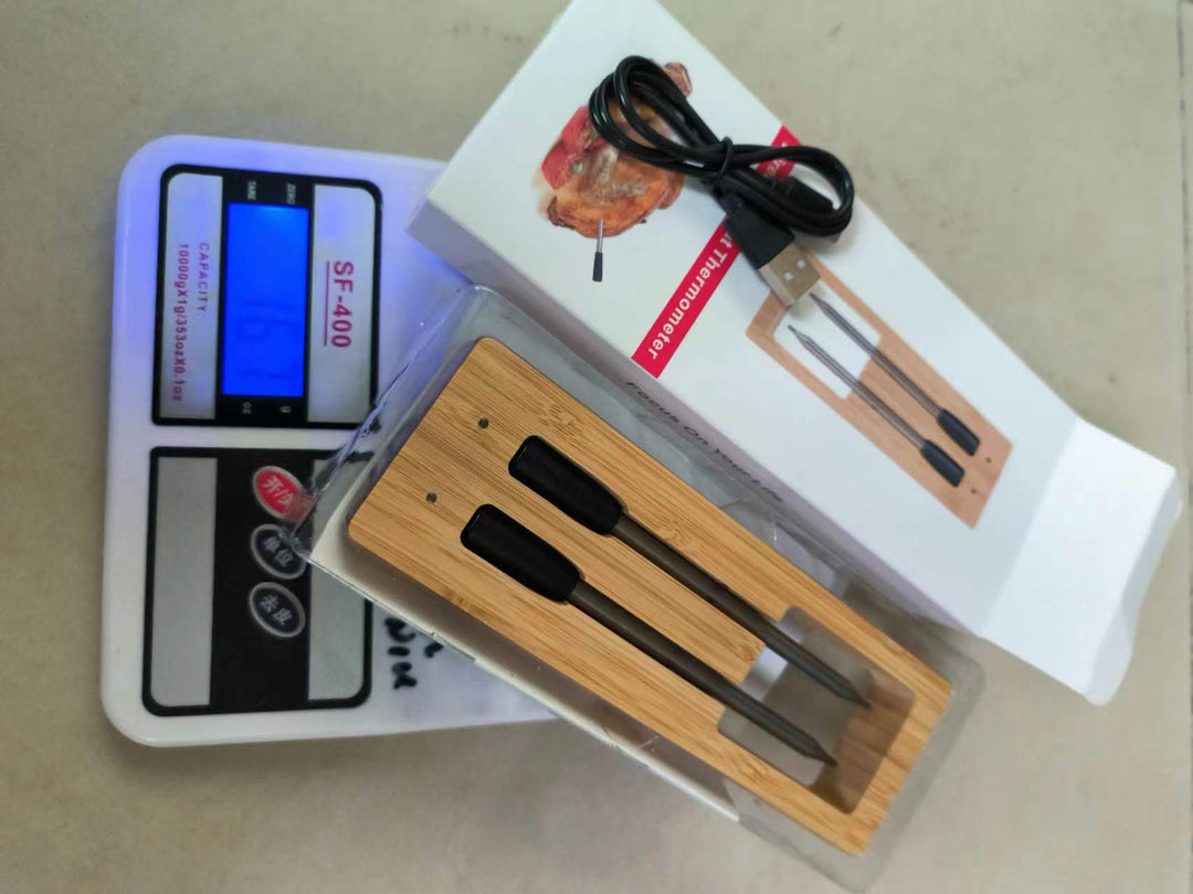 Kötttermometer i förpackning placerad på en digital våg med medföljande laddkabel