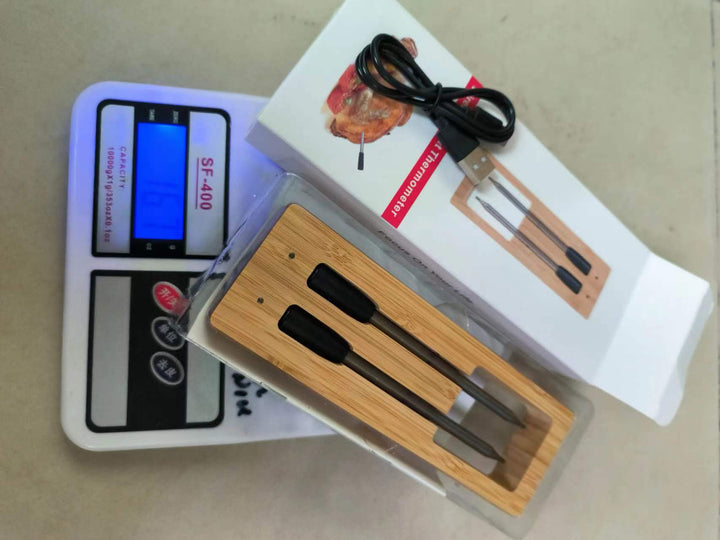 Kötttermometer i förpackning placerad på en digital våg med medföljande laddkabel
