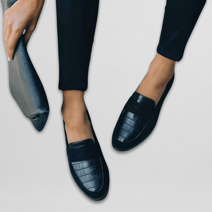 Modell som håller en matchande svart accessoar bredvid loafers