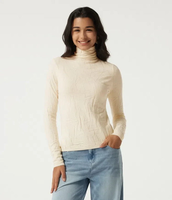 Kvinna som bär en beige långärmad tröja med hög hals framifrån