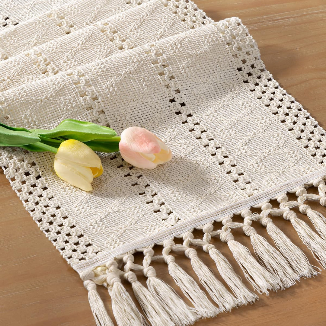 Närbild på en beige makramébordslöpare med handknutna tofsar och vårblommor på träbord