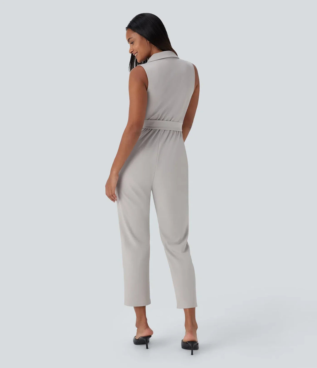 Kvinna i ljusgrå ärmlös bältad arbetsjumpsuit bakifrån
