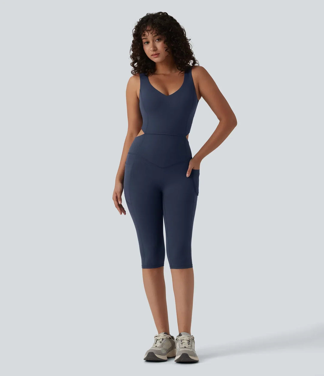 Frammifrån vy av blå träningsjumpsuit med V-ringning och sidofickor på modell