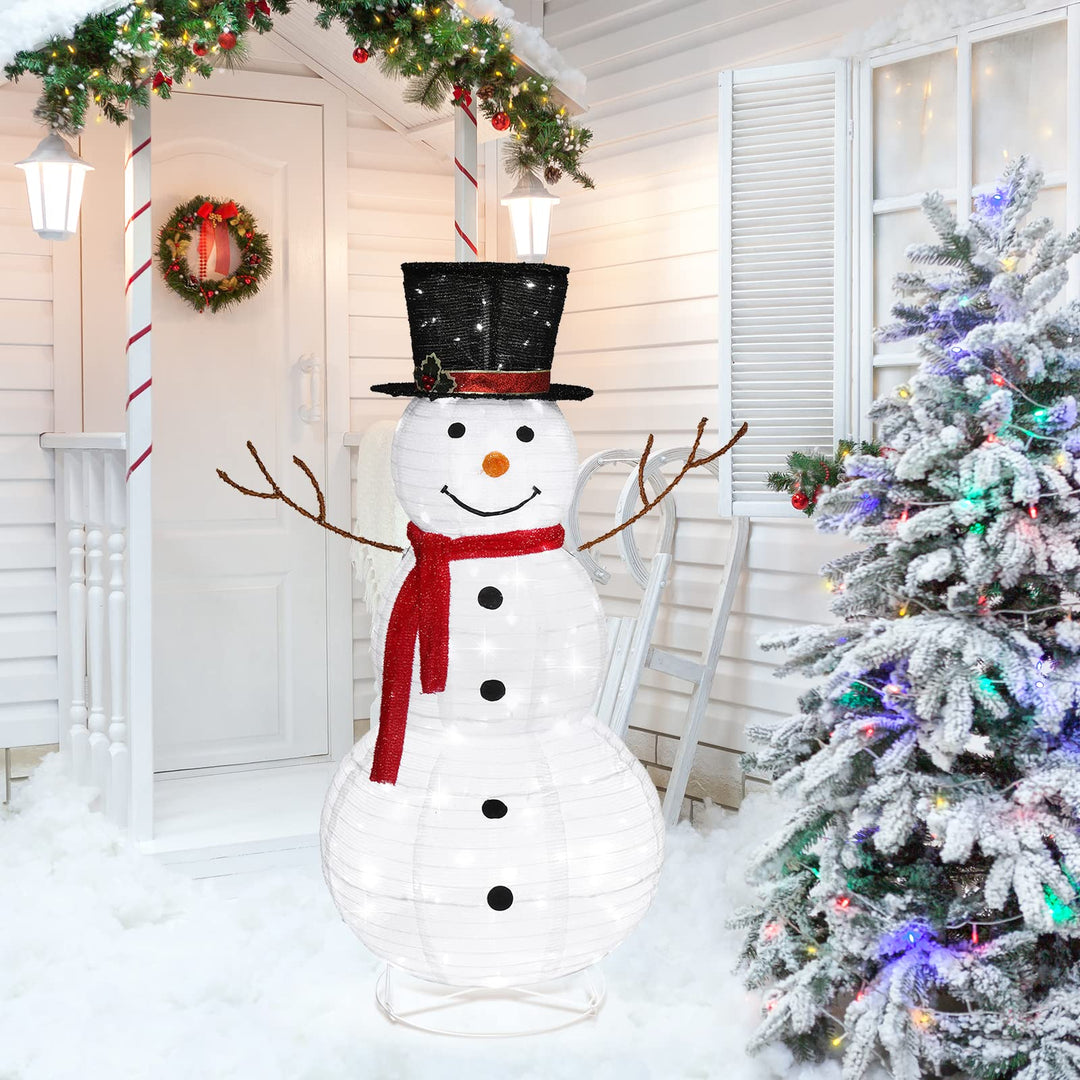 Traditionell upplyst LED-snögubbe med röd halsduk och svart hatt på verandan.