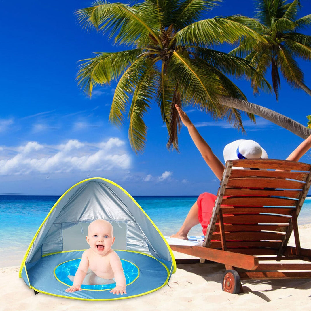 Barn i säkert UV-tält med minipool en solig sommardag på stranden