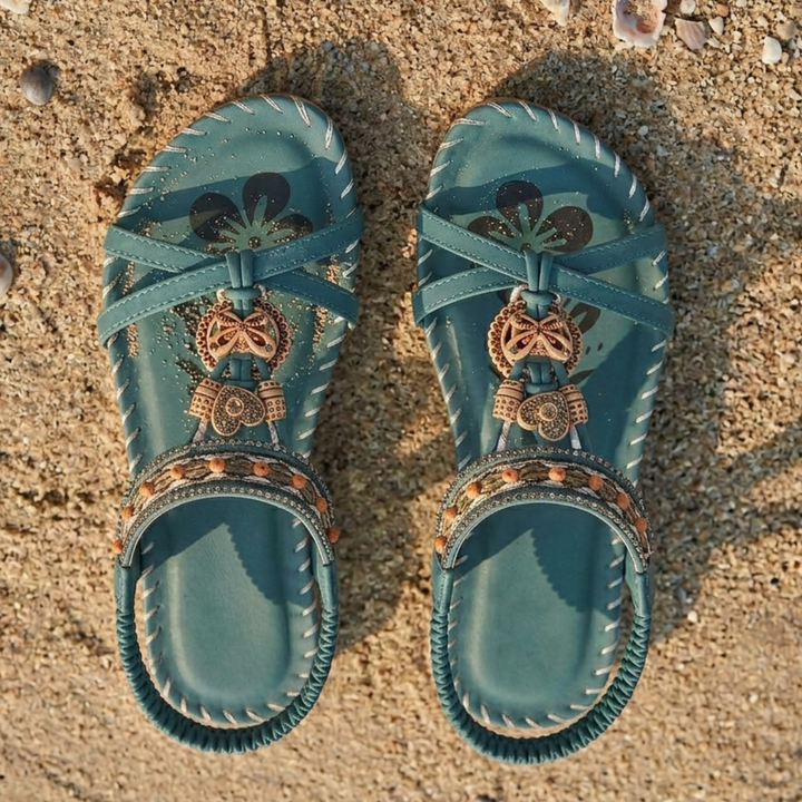 Par mörkgröna sandaler placerade på sandstrand