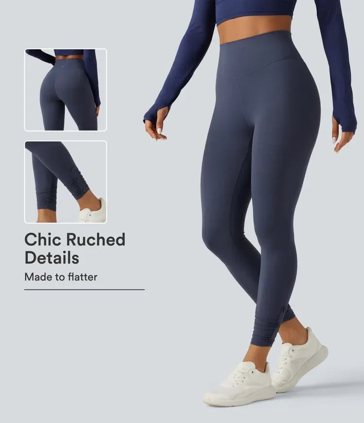 Dam i mörkblå höga yogaleggings med rynkade detaljer och vita sneakers