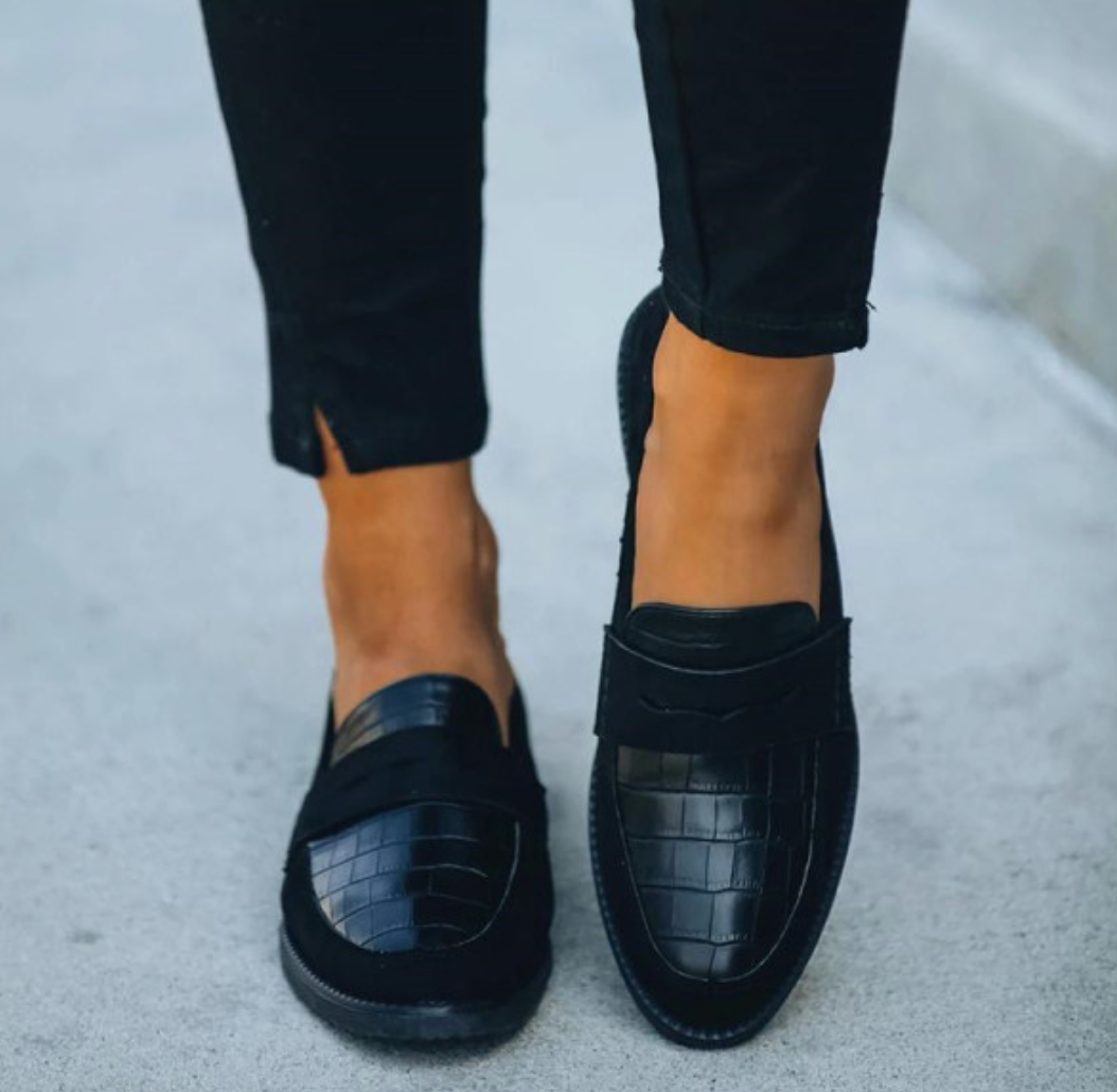 Svarta damloafers med texturerad finish framifrån bärna med svarta byxor