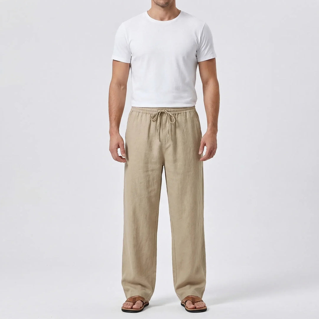 Helbild framifrån av man iklädd vida sommarbyxor i khaki och vit t-shirt mot neutral bakgrund