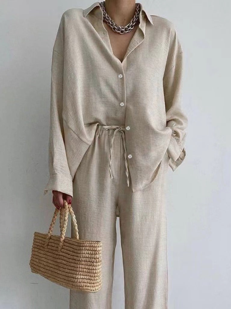 Kvinna i beige blus och matchande byxor med vida ben som håller en handväska