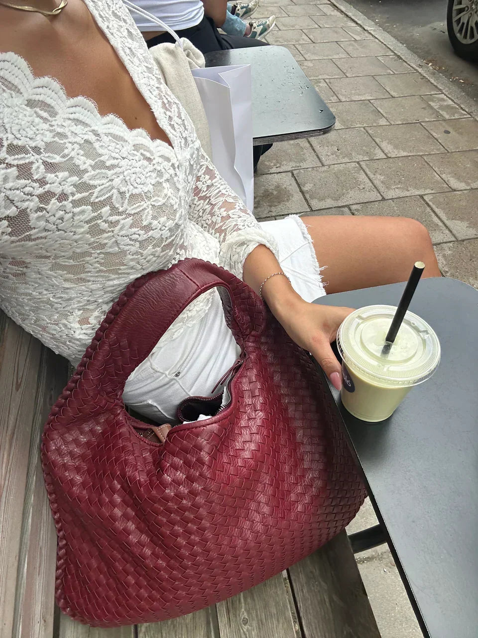 Kvinna som sitter på uteservering med röd flätad totesväska