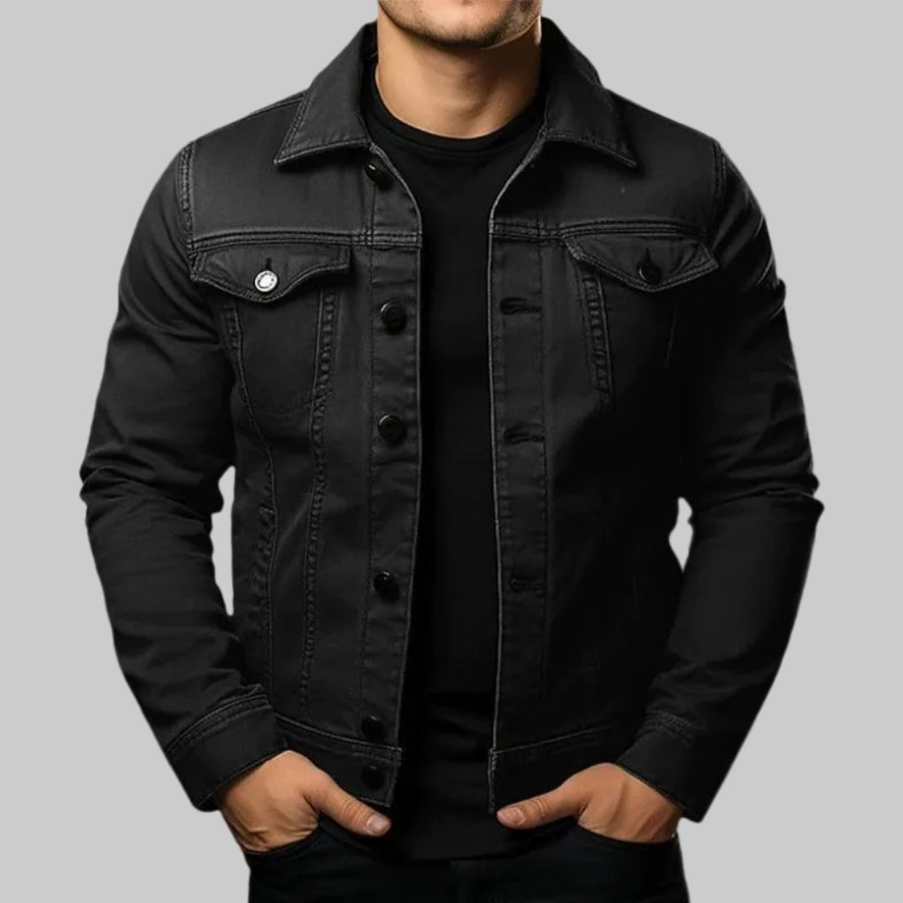 Man bär en svart denimjacka mot en neutral bakgrund