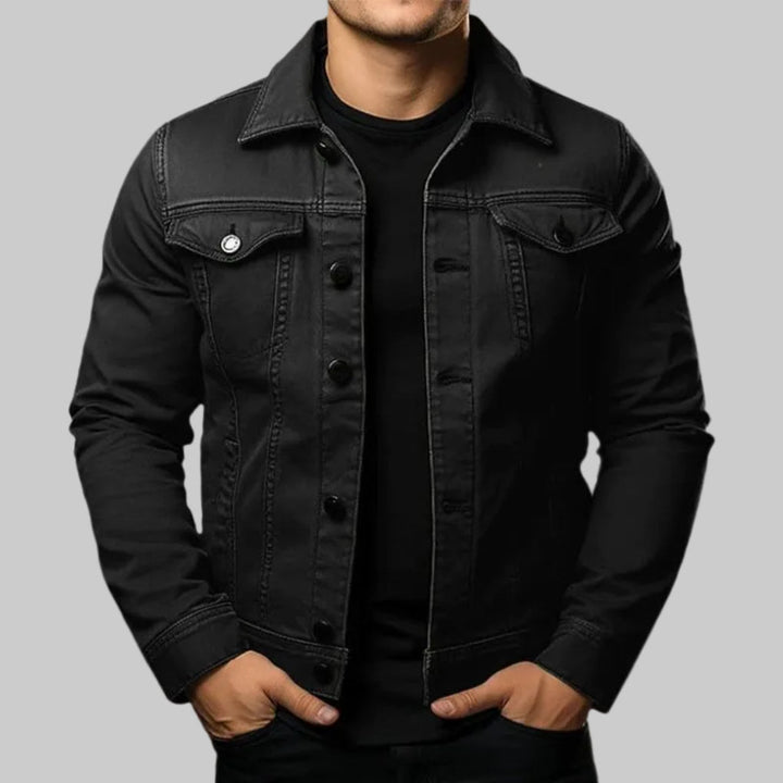 Man bär en svart denimjacka mot en neutral bakgrund