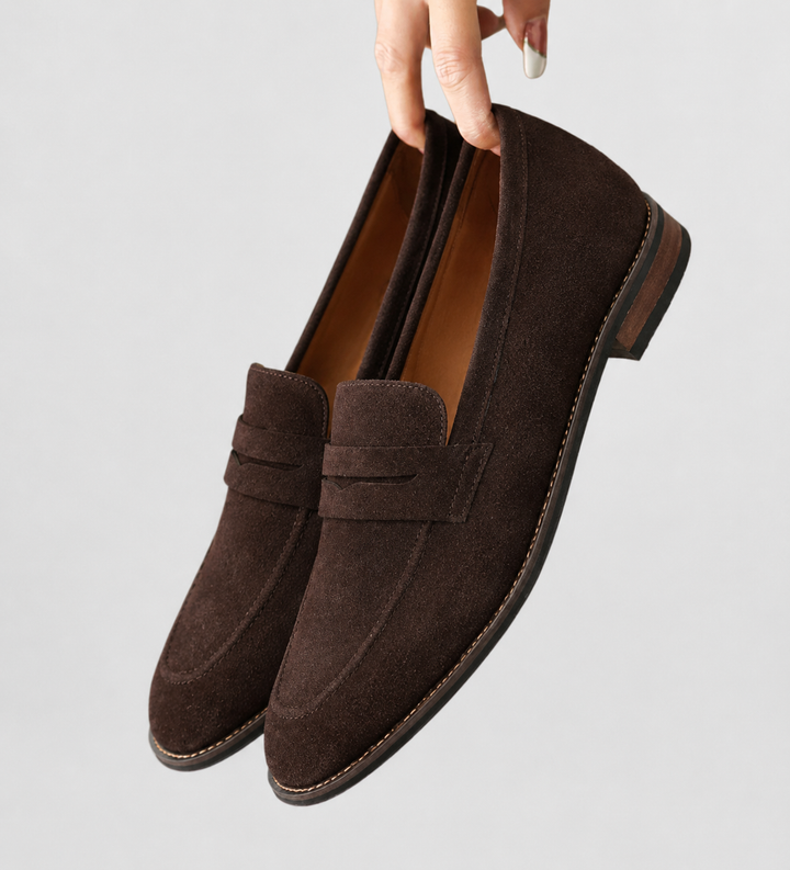 Mörka dam loafers i klassisk stil som hålls upp mot en neutral bakgrund