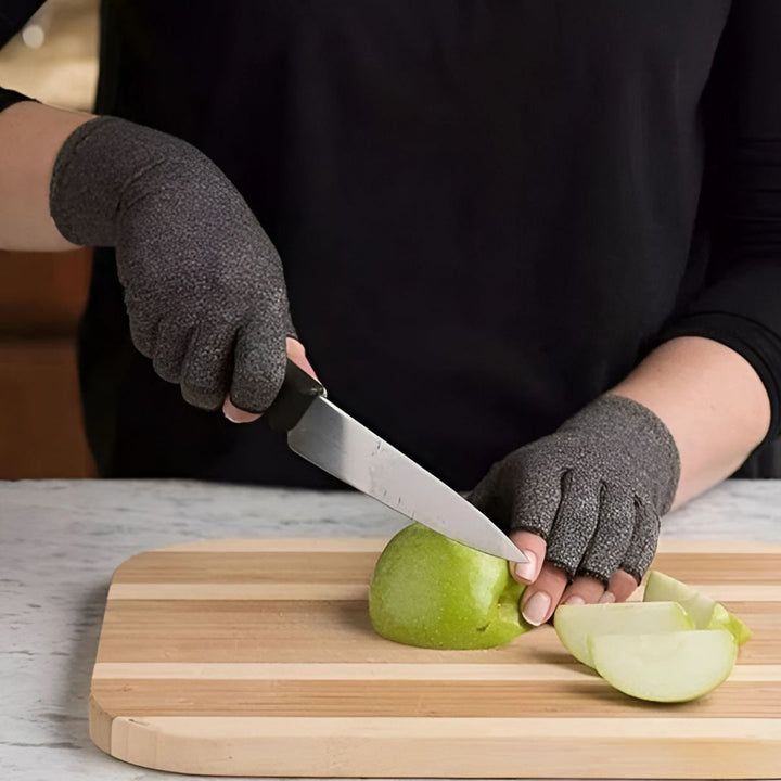 Person som bär grå termohandskar med öppna fingrar medan de skär ett äpple på en skärbräda