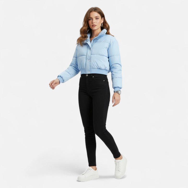 Modell som bär ljusblå damjacka med svarta byxor och vita sneakers