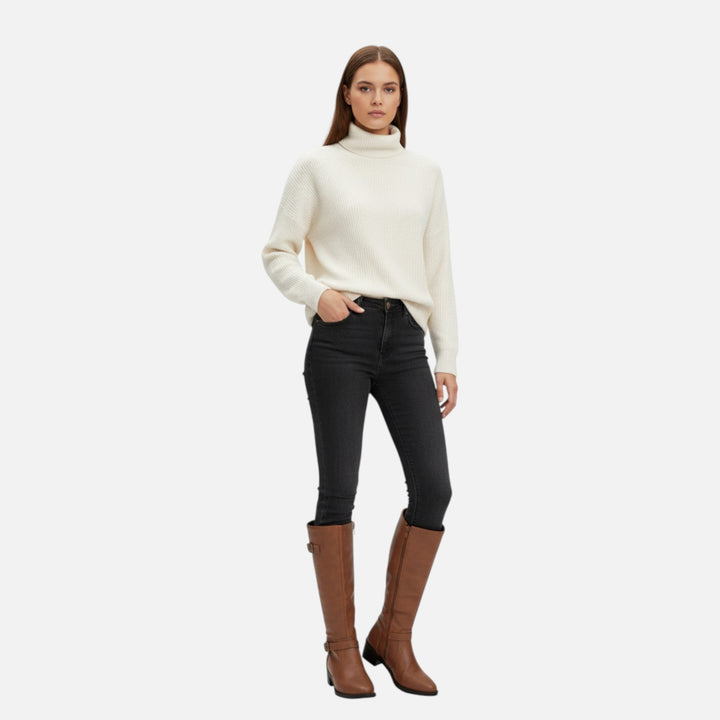 Kvinna i vit polotröja och svarta jeans som bär bruna långa damstövlar