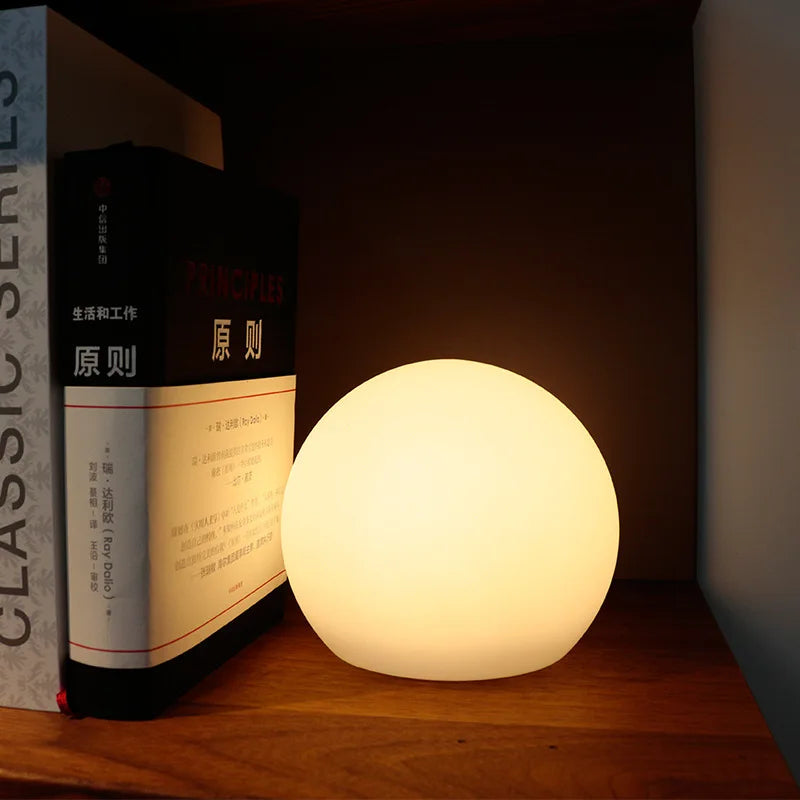Trådlös LED-globlampa placerad bredvid böcker på ett träbord