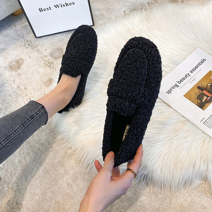 Svart damloafer med fluffig textur hålls i handen ovanför en matta