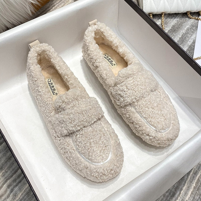Två beige damloafers i plysch placerade i en presentask