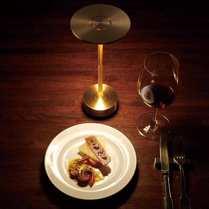 Trådlös skrivbordslampa i guld placerad bredvid en elegant tallrik